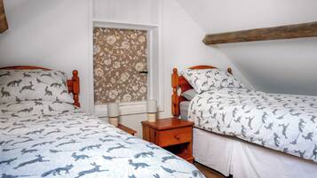 A bedroom with two beds, a window with floral wallpaper, and a wooden ceiling beam.
