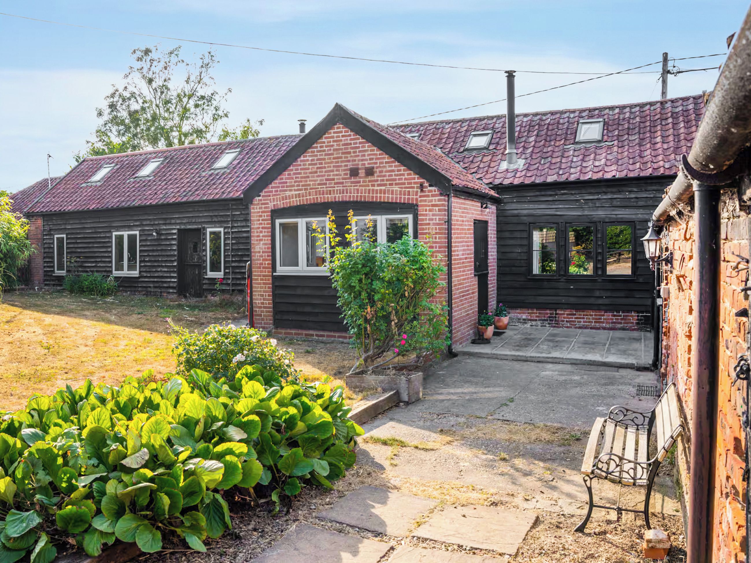 A two-story house with a brick facade, a red-tiled roof, and a small garden with green plants.