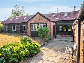 Een tweelaags huis met een bakstenen gevel, een dak met rode tegels en een kleine tuin met groene planten.