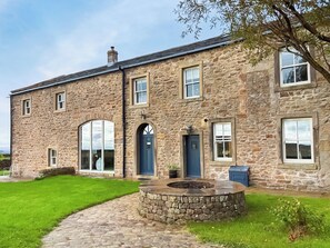 A stone building with a circular stone fire pit, a blue door, and a small garden area. - 5 bedroom accommodation in Long Preston (Long Preston)