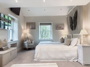Ein Schlafzimmer mit einem großen Bett, zwei Nachttischen, einem Sessel, einem Fenster und Bildern an den Wänden.