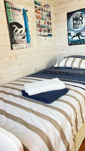 A bed with striped bedding, a folded towel, and posters on the wall. - Charming, renovated Penty, 250 meters from the sea, the Eckmühl Lighthouse, and Pointe de la Torche (Penmarch)
