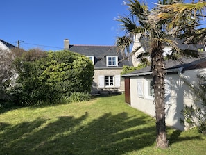 A stone house with a thatched roof, surrounded by a well-maintained lawn and a variety of shrubs. - Charming, renovated Penty, 250 meters from the sea, the Eckmühl Lighthouse, and Pointe de la Torche (Penmarch)