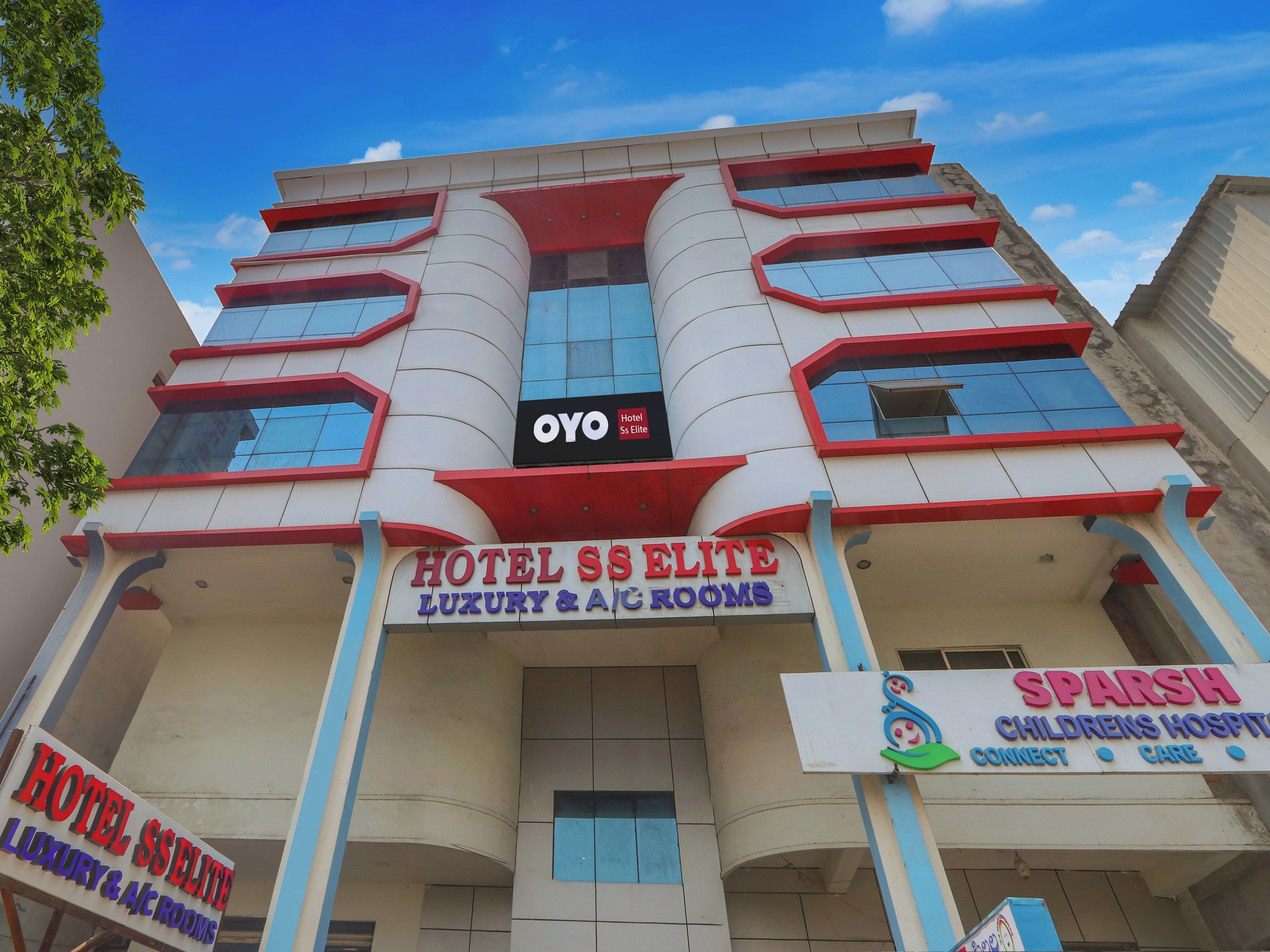 Un edifici de diverses plantes amb un cartell destacat per 'Hotel Sse Elite Luxury & A/C Rooms' i un cartell més petit per 'Sparsh Childrens Hospital Connect Care'.