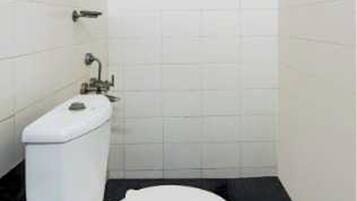 A small, compact bathroom with a white toilet, a shower area, and a window with blinds.