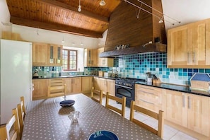 A kitchen with wooden cabinets, a tiled backsplash, and a dining table with chairs. - Le pied a terre - 6 or 8 people (MONTFERRAND DU PERIGORD)