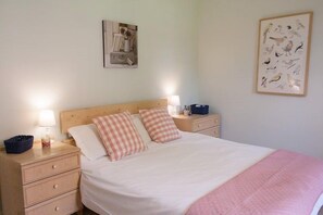 A neatly made bed with checkered pillows, a bedside table with a lamp, and a wall with framed artwork. - Le pied a terre - 6 or 8 people (MONTFERRAND DU PERIGORD)