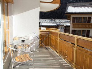Ein Balkon mit Tisch und Stühlen, einem Hollerleger und Blick auf schneebedeckte Gebäude.