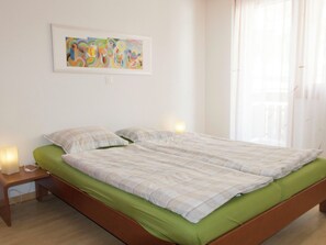 Ein Zimmer mit einem Einzelbett, einer grünen Tagesdecke, einem Nachttisch mit Lampe und einem farbenfrohen abstrakten Bild an der Wand.