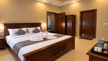Une chambre d’hôtel avec un grand lit, un ventilateur de plafond, une table de chevet et une petite table de nuit avec un plateau contenant des articles de toilette, ainsi qu’une armoire en bois.