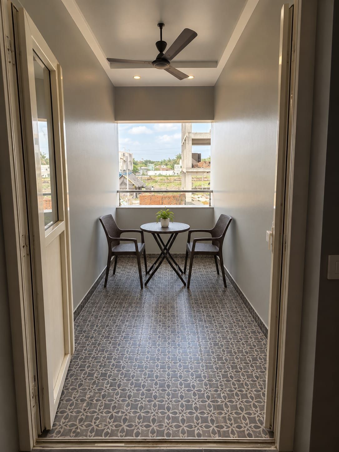Ein schmaler Korridor mit Deckenventilator, einem kleinen Tisch mit zwei Stühlen und einem Fenster mit Blick auf Gebäude und Grünflächen.