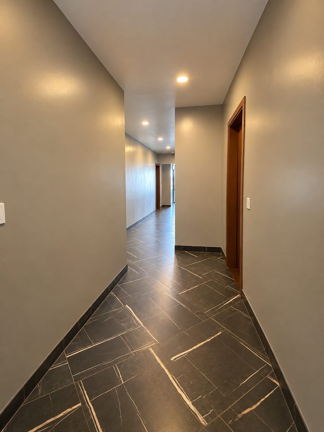 Un couloir au sol carrelé, avec une porte en bois sur le côté droit.