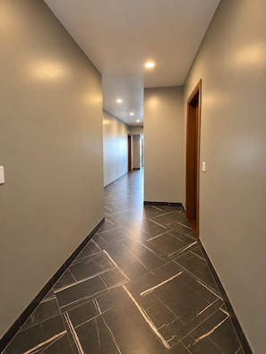 A corridor with a tiled floor and a wooden door on the right. - Hotel Grand Mirage (Chennai)