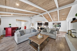 A spacious living area with a high ceiling, wooden beams, and a kitchen in the background. - South Lake Tahoe • Fireplace + Pine-View Deck + Trail Access | Timberlight (South Lake Tahoe)