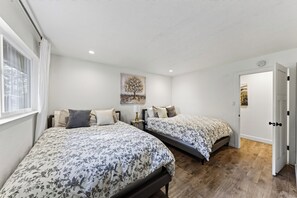 A bedroom with two beds, a painting on the wall, and a door leading to another room. - South Lake Tahoe • Fireplace + Pine-View Deck + Trail Access | Timberlight (South Lake Tahoe)
