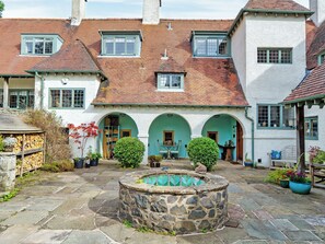 A courtyard with a stone fountain, a wooden bench, and a building with multiple arches and windows. - Lady Bluebell - UKC10036 (St Andrews)