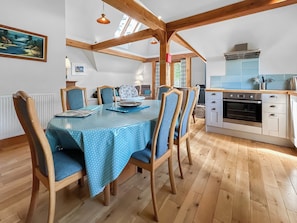 Un coin repas avec une table dressée pour quatre personnes, des chaises en bois, une cuisine équipée d’une cuisinière et de placards, et une lucarne au-dessus.