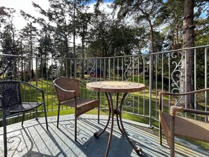 Une terrasse avec une table ronde et deux chaises en osier, entourée d’une clôture en métal et d’arbres.
