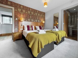 Une chambre d’hôtel avec deux lits, un grand miroir, une tête de lit en bois et une salle de bain équipée d’un lavabo et d’une douche.
