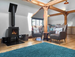 Un salon chaleureux avec un poêle à bois, deux fauteuils en cuir, un tapis bleu et une structure de plafond en bois.