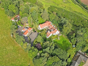 An aerial view of a residential area with multiple houses, a parking area, and surrounding greenery. - Red Squirrel Cottage Apartment - UKC10040 (St Andrews)