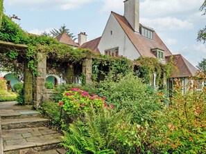 A traditional house with a stone staircase leading to a door, surrounded by lush greenery and flowering plants. - Baillie Scott Cottage - UKC10041 (St Andrews)