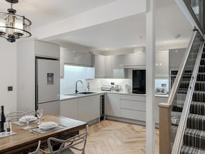 A modern kitchen with white cabinetry, a wooden dining table, and a staircase leading to another level. - 3 bedroom accommodation in Eyemouth (Eyemouth)