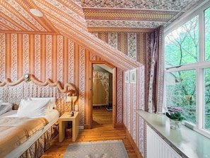 A room with patterned wallpaper, a bed, a nightstand, a lamp, and a window with a view of greenery. - 1 bedroom accommodation in Bishops Castle (Bishops Castle)
