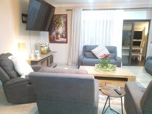Ein Wohnzimmer mit Sofa, Sessel, Couchtisch und einem an der Wand befestigten Flachbildfernseher.