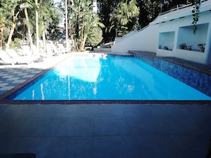 A swimming pool with a tiled edge, surrounded by potted plants and trees. - Luxurious 6-Bedroom House with Private Facilities in Ugu District (Ugu District Municipality)