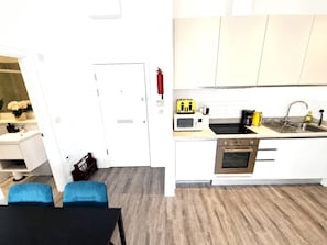 Eine moderne Küche mit weißen Schränken, einer Mikrowelle, einem Herd und einem Spülbecken. An der Wand ist ein Feuerlöscher angebracht.