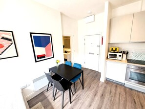 Eine moderne Küche mit Mikrowelle, Toaster und Backofen. Ein Essbereich mit einem schwarzen Tisch und blauen Stühlen.
