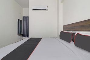 Une chambre d’hôtel avec un lit, une fenêtre avec des rideaux, un appareil de climatisation et une tête de lit en bois.
