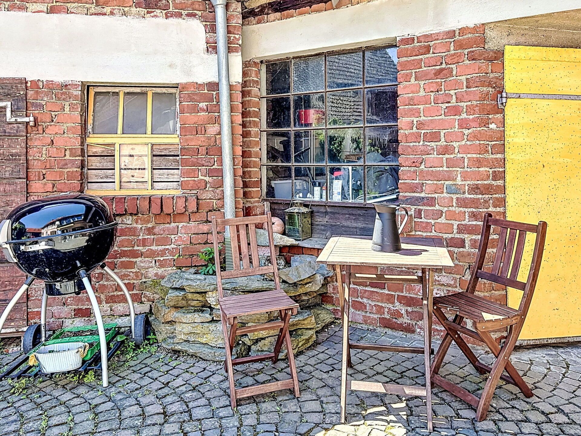 An outdoor seating area with a brick wall, a yellow door, and a grill.