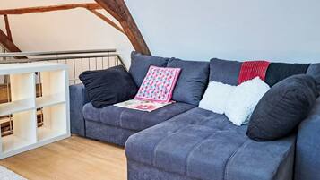 A grey sofa with black and white cushions, a pink patterned throw, and a red and black striped blanket.