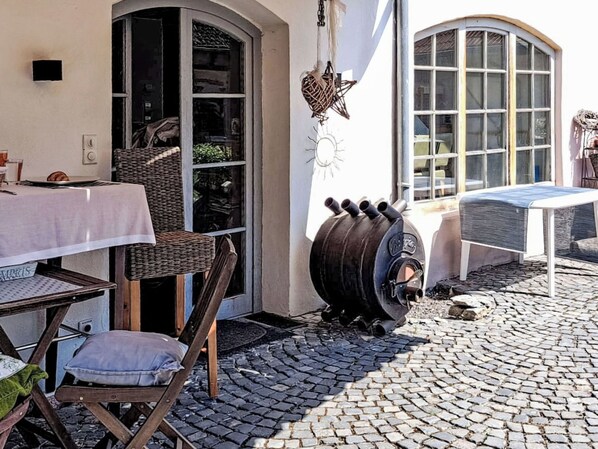 A cobblestone patio with outdoor furniture, a large barrel, and a building with a curved window.