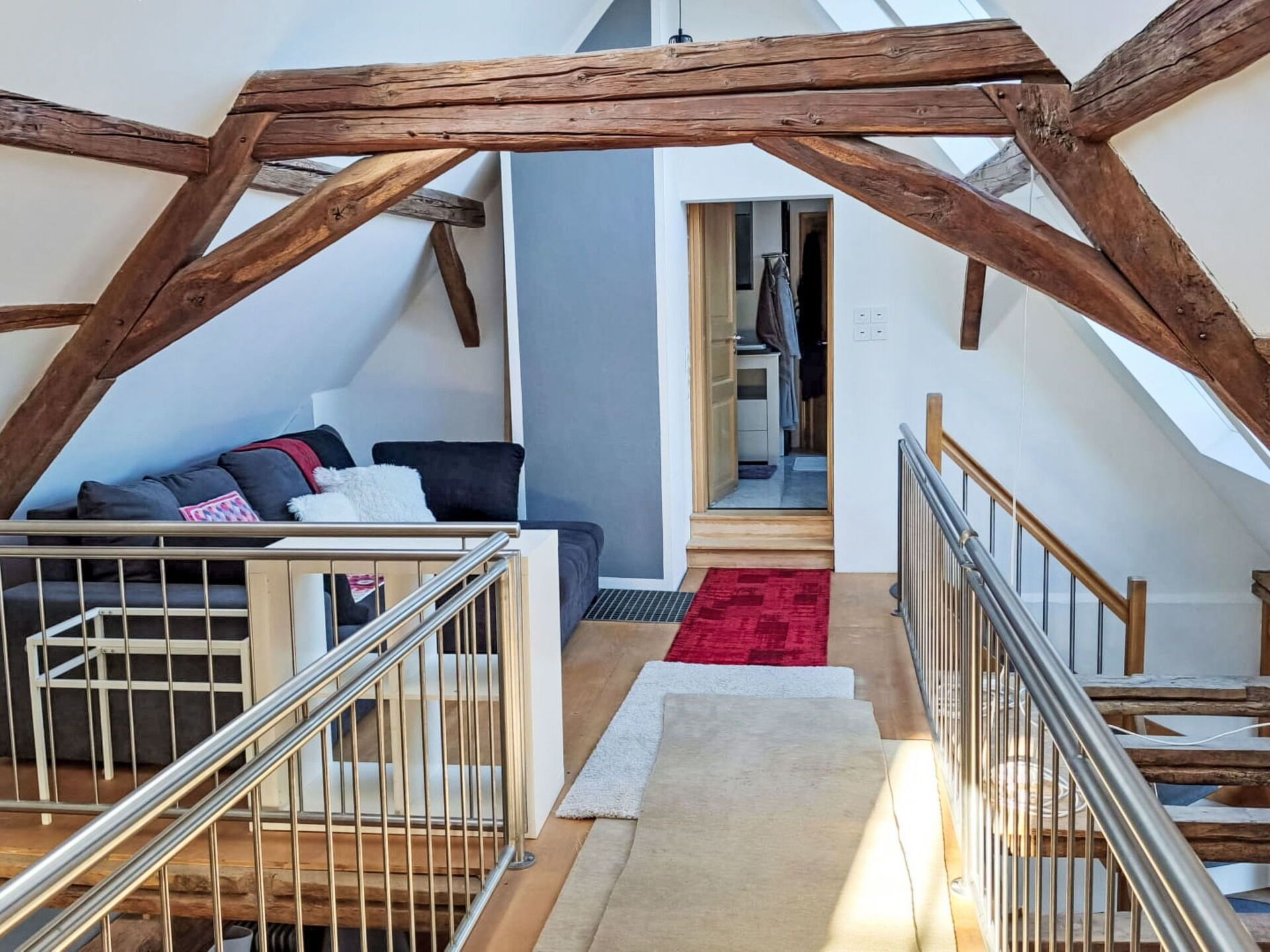 Une pièce de style « loft », avec un plafond haut, des poutres apparentes, un escalier et une vue sur une chambre avec un placard.