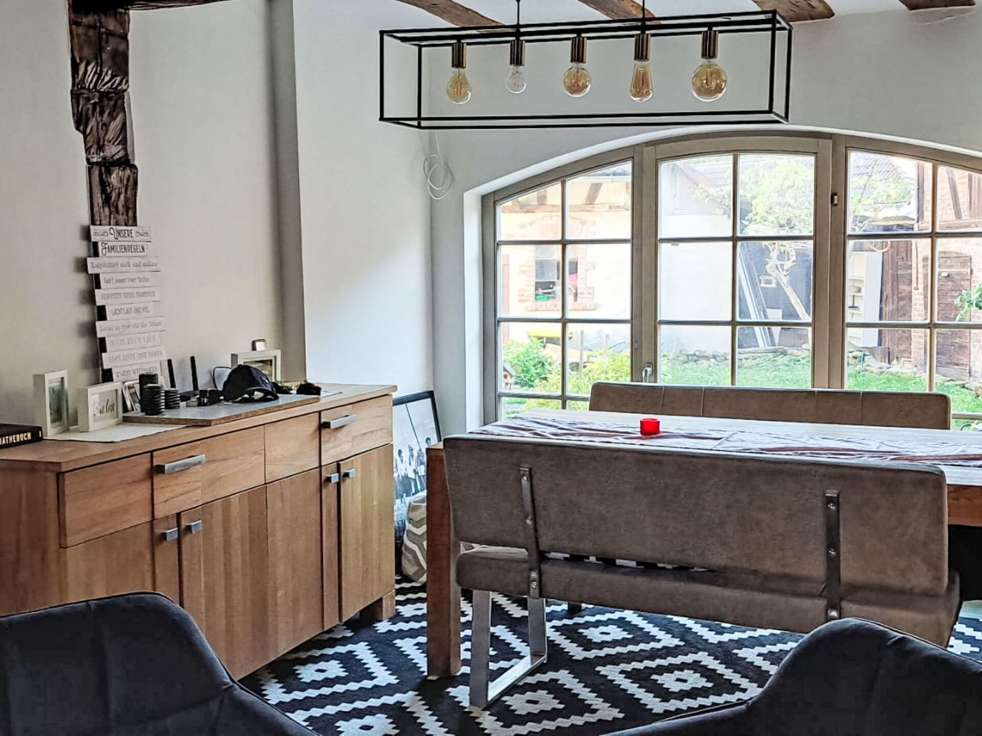 Ein Essbereich mit Tisch und Stühlen, einer Holzschrank und einem Fenster mit Blick auf Grünflächen.
