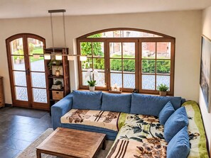 Ein Wohnzimmer mit einem blauen Sofa, einem Holztisch und Blick durch große Bogenfenster.