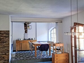 Ein gemütlicher Raum mit Esstisch, Stühlen, einer kleinen Küchenzeile und einem großen Fenster für natürliches Licht.