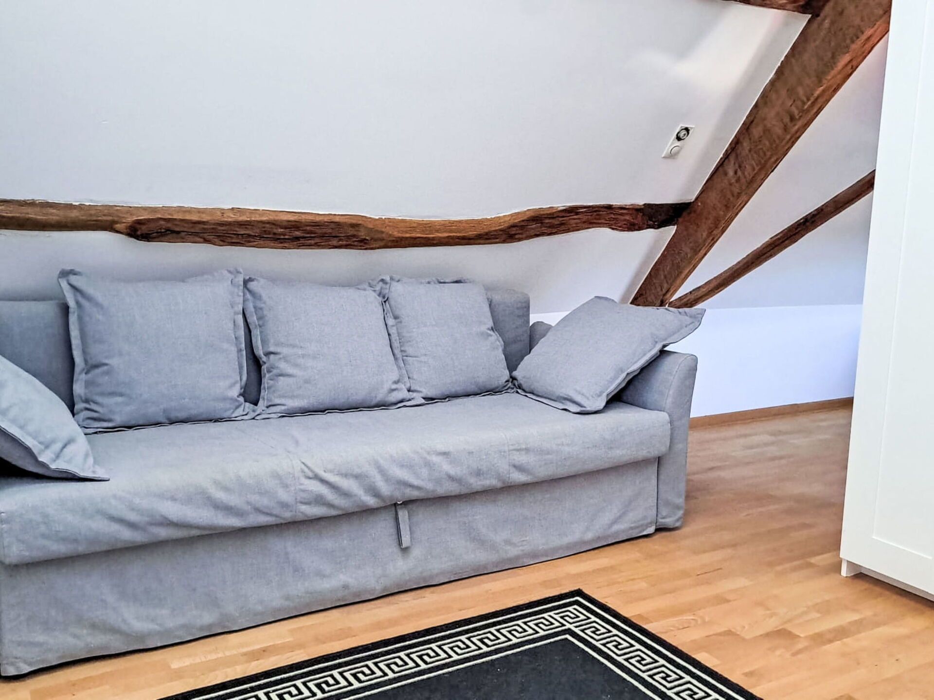 Un canapé gris avec des coussins, dans une pièce dotée de poutres en bois et d’un tapis à motifs.