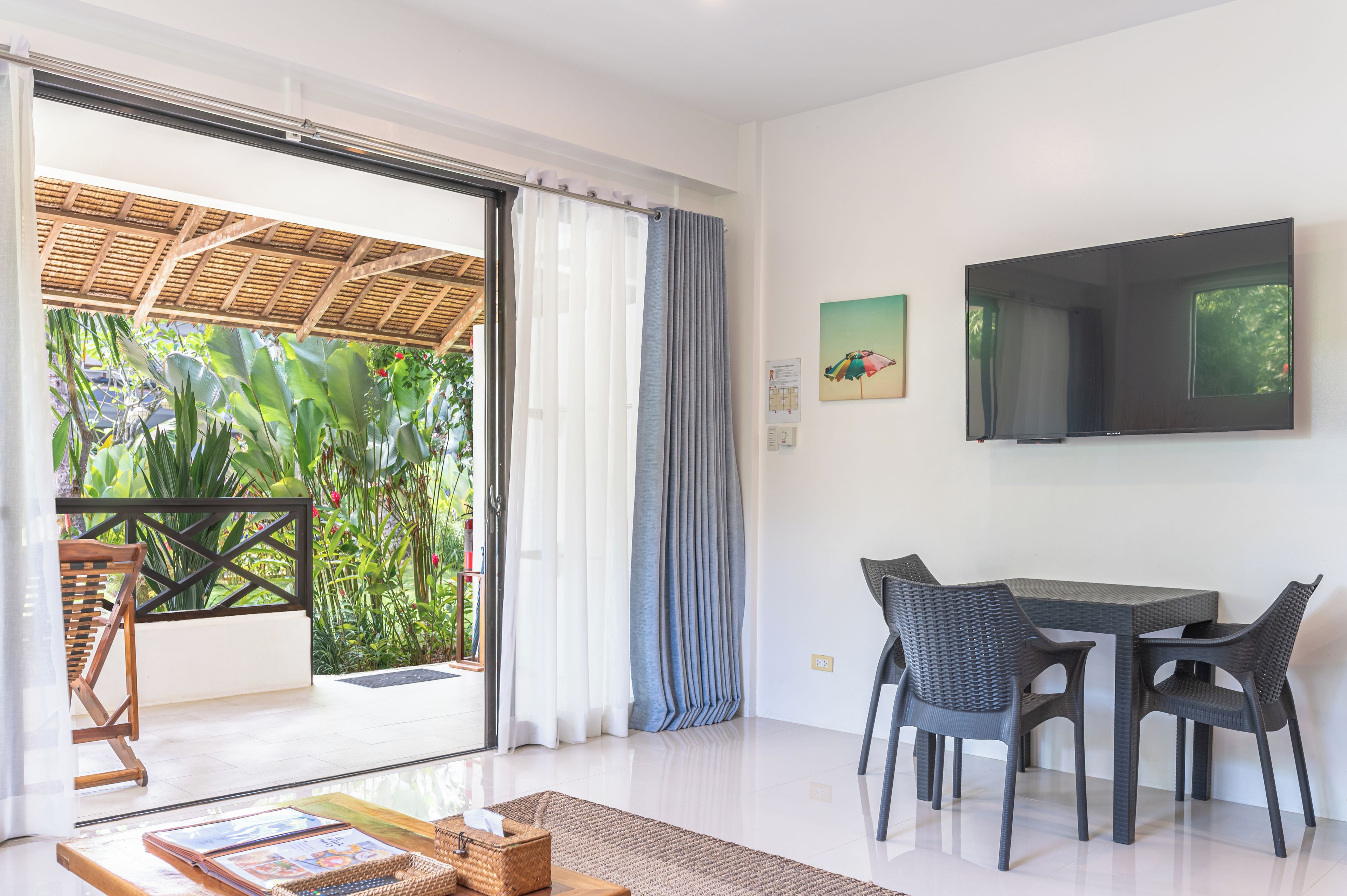 A modern room with a sliding glass door leading to a balcony, a flat-screen TV mounted on the wall, and a dining area with a table and chairs.