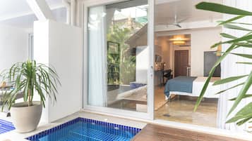 Camera d'hotel moderna con una porta scorrevole in vetro che dà su un balcone, una piccola piscina e un letto con copriletto blu.