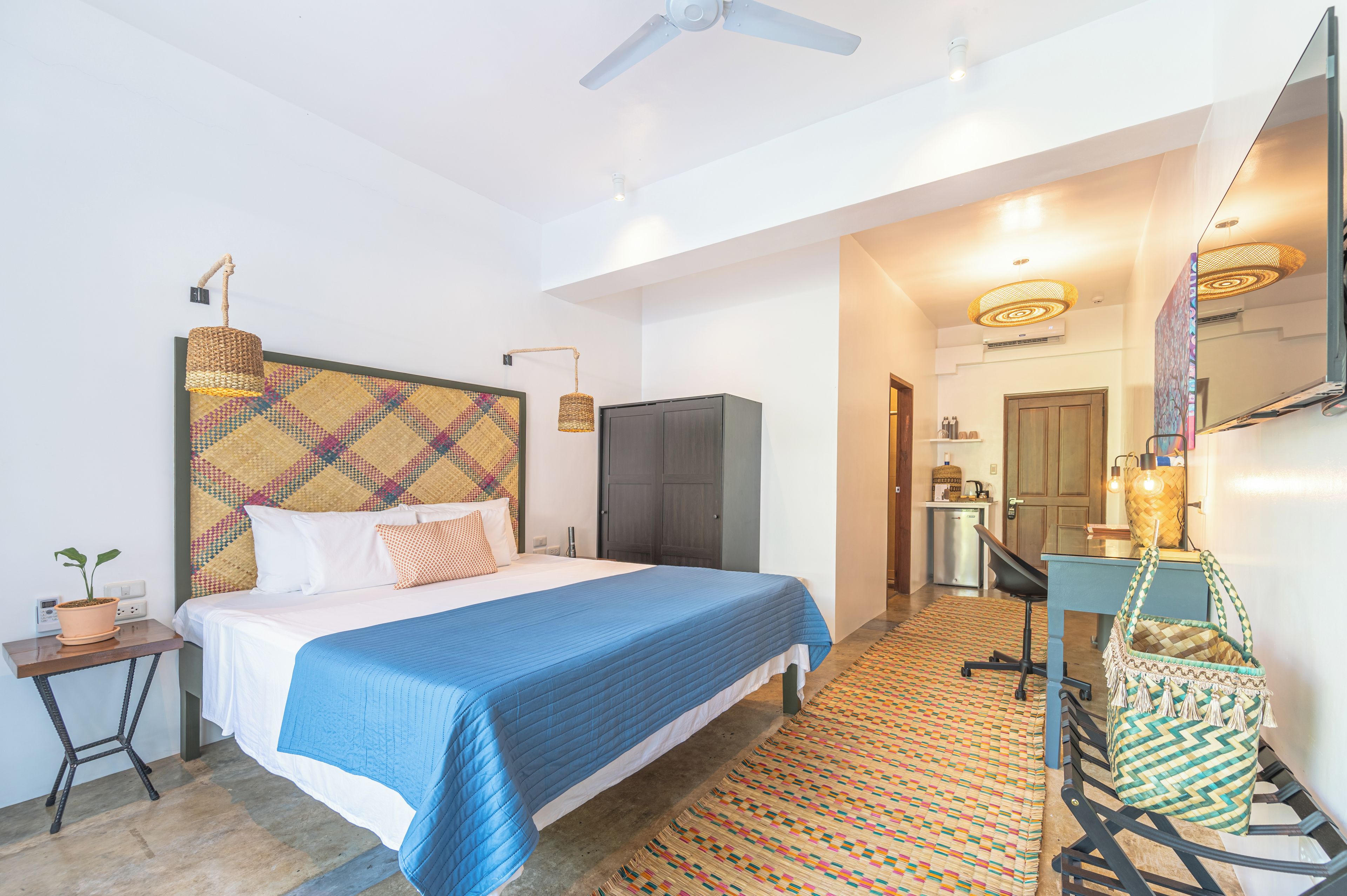 Een hotelkamer met een bed, een bureau, een stoel, een kledingkast, een plafondventilator en een vloer met een patroon.