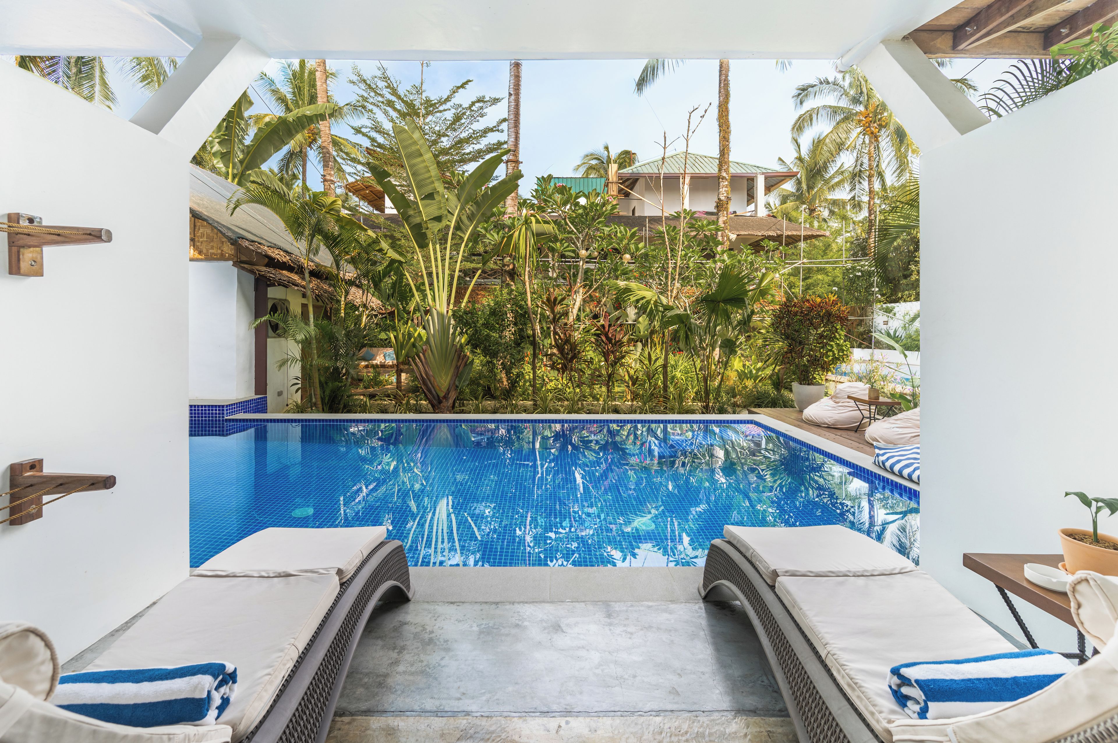 Un área de piscina con dos sillas de descanso, una piscina azul cristalina y vegetación tropical circundante.
