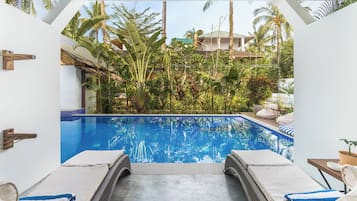 Un área de piscina con dos sillas de descanso, una piscina azul cristalina y vegetación tropical circundante.