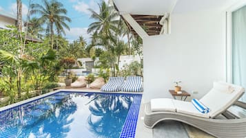 Area piscina con vasca azzurra trasparente, sedie a sdraio e vegetazione tropicale.