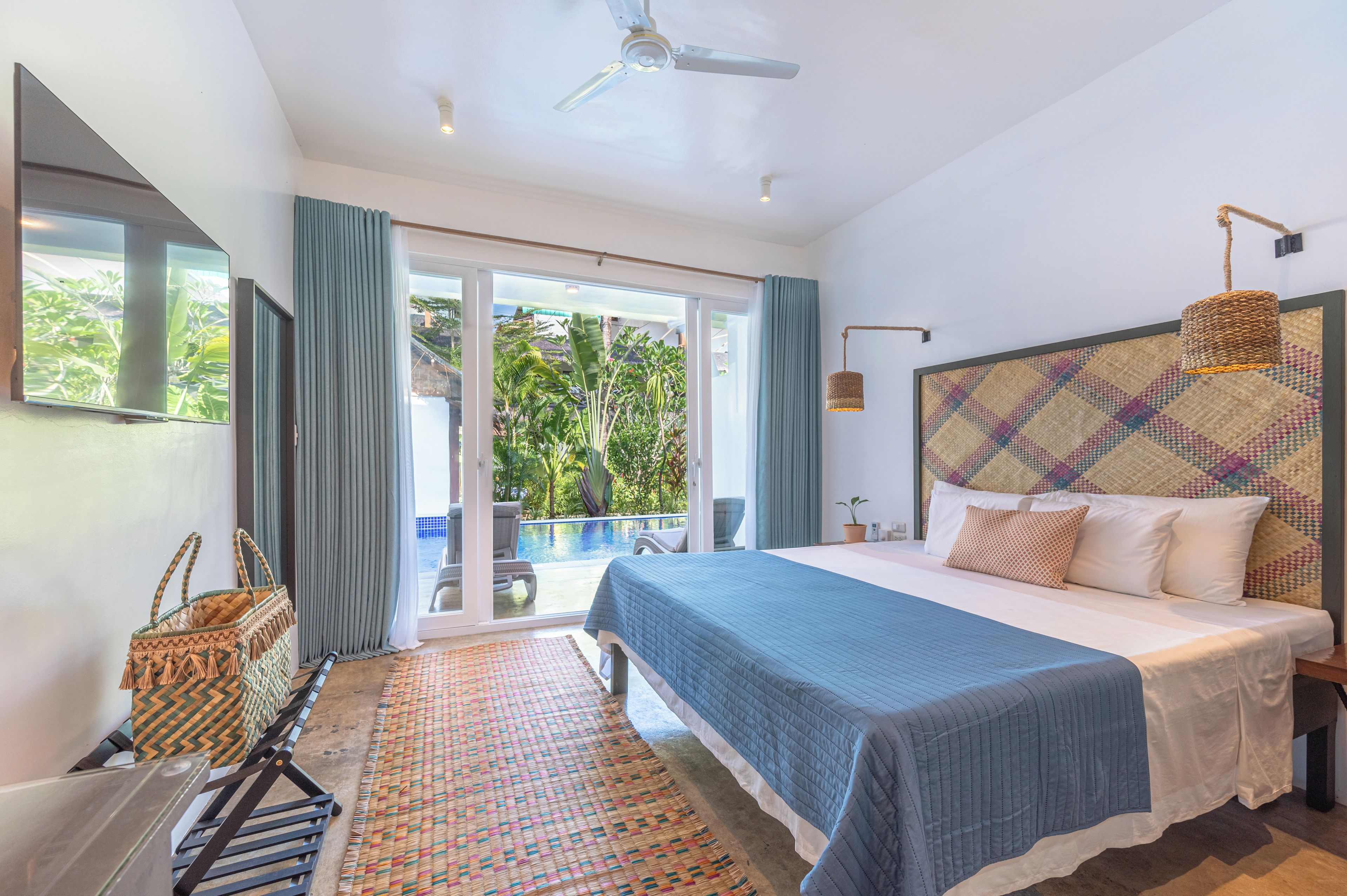 A bedroom with a large bed, a ceiling fan, a view of the outdoors, and a sliding glass door.