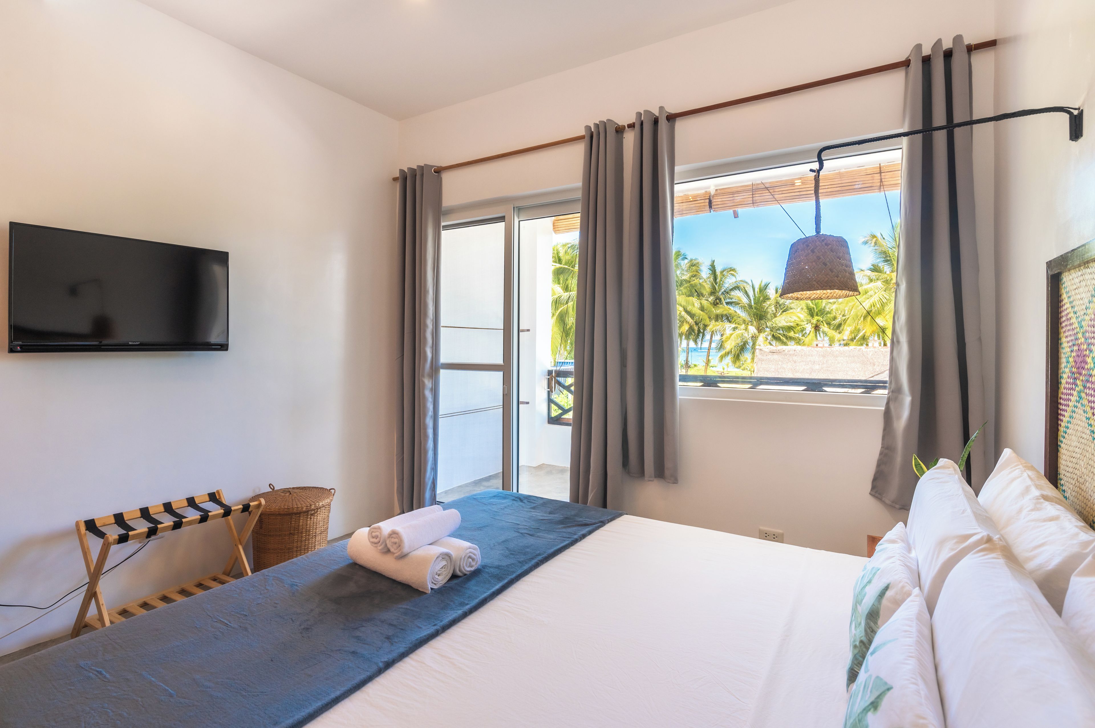 A hotel room with a bed, a flat-screen TV, a view of palm trees, and a balcony.