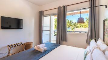 A hotel room with a bed, a flat-screen TV, a view of palm trees, and a balcony.